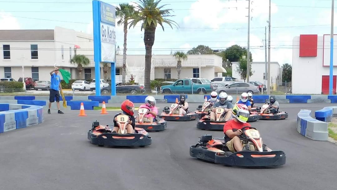 Kart racers in helmets lined up on an indoor track